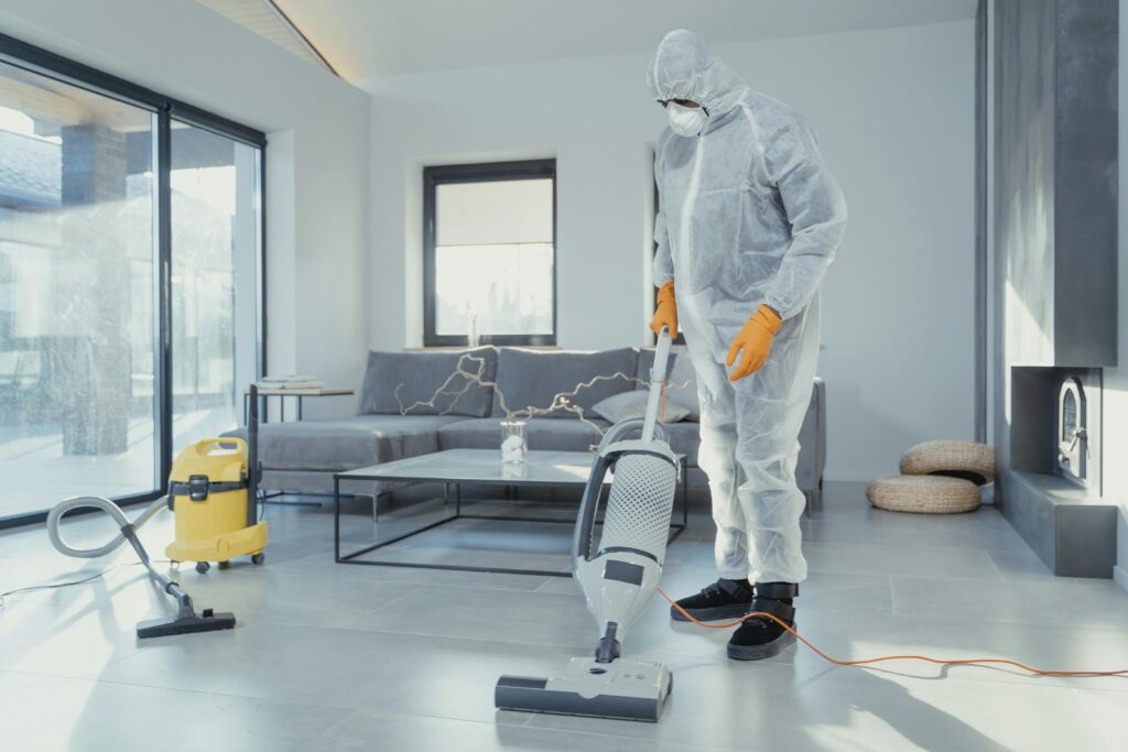 Man in White Robe and White Pants Standing Beside Gray Vacuum Cleaner